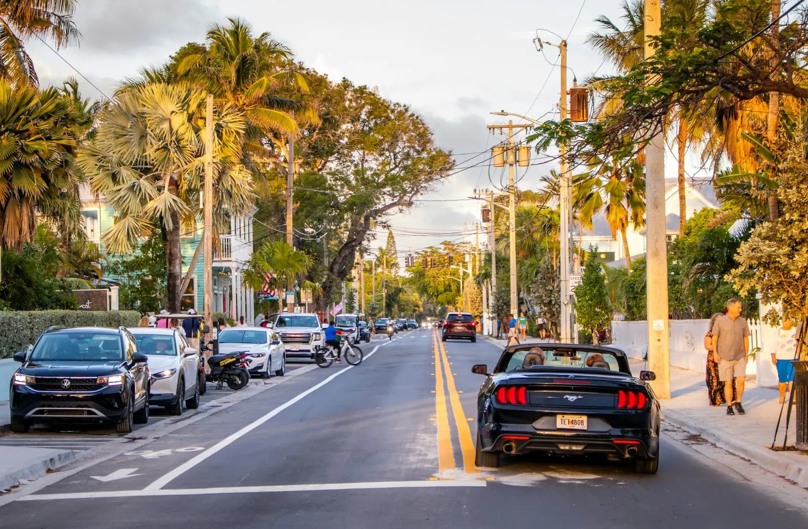 Key West’te palmiyeli bir cadde; kaldırım boyunca park etmiş arabalar ve yoldan geçen üstü açık bir otomobil.