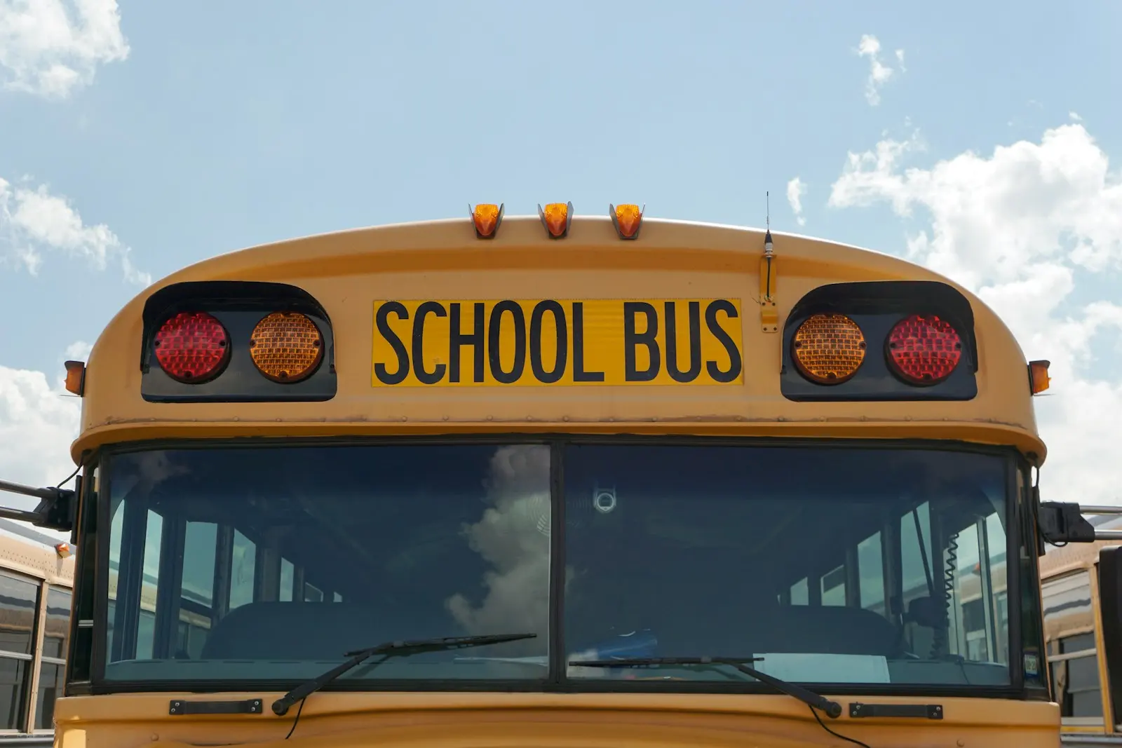 Önden yakın planda sarı bir okul otobüsü; ön camın üstünde “SCHOOL BUS” yazısı.